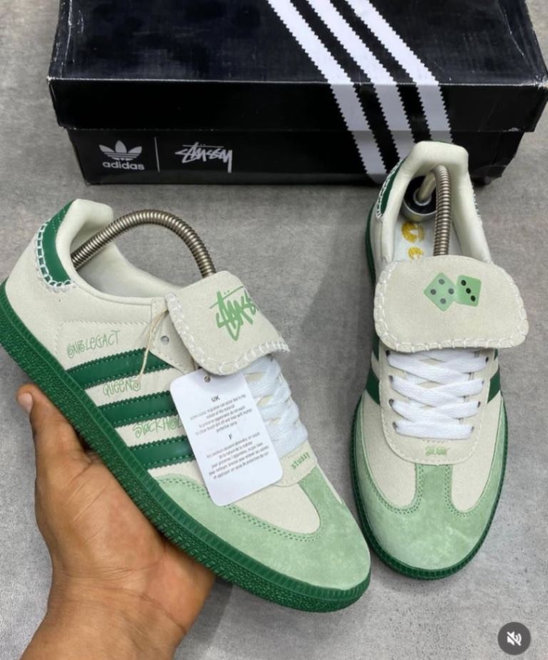 Adidas x Stussy Samba sneakers feature a distinctive green and white suede upper with a folding tongue detail.